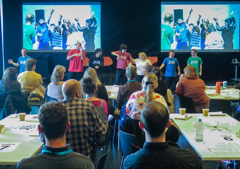 Seven Jolt dancers present to an audience, stand in from